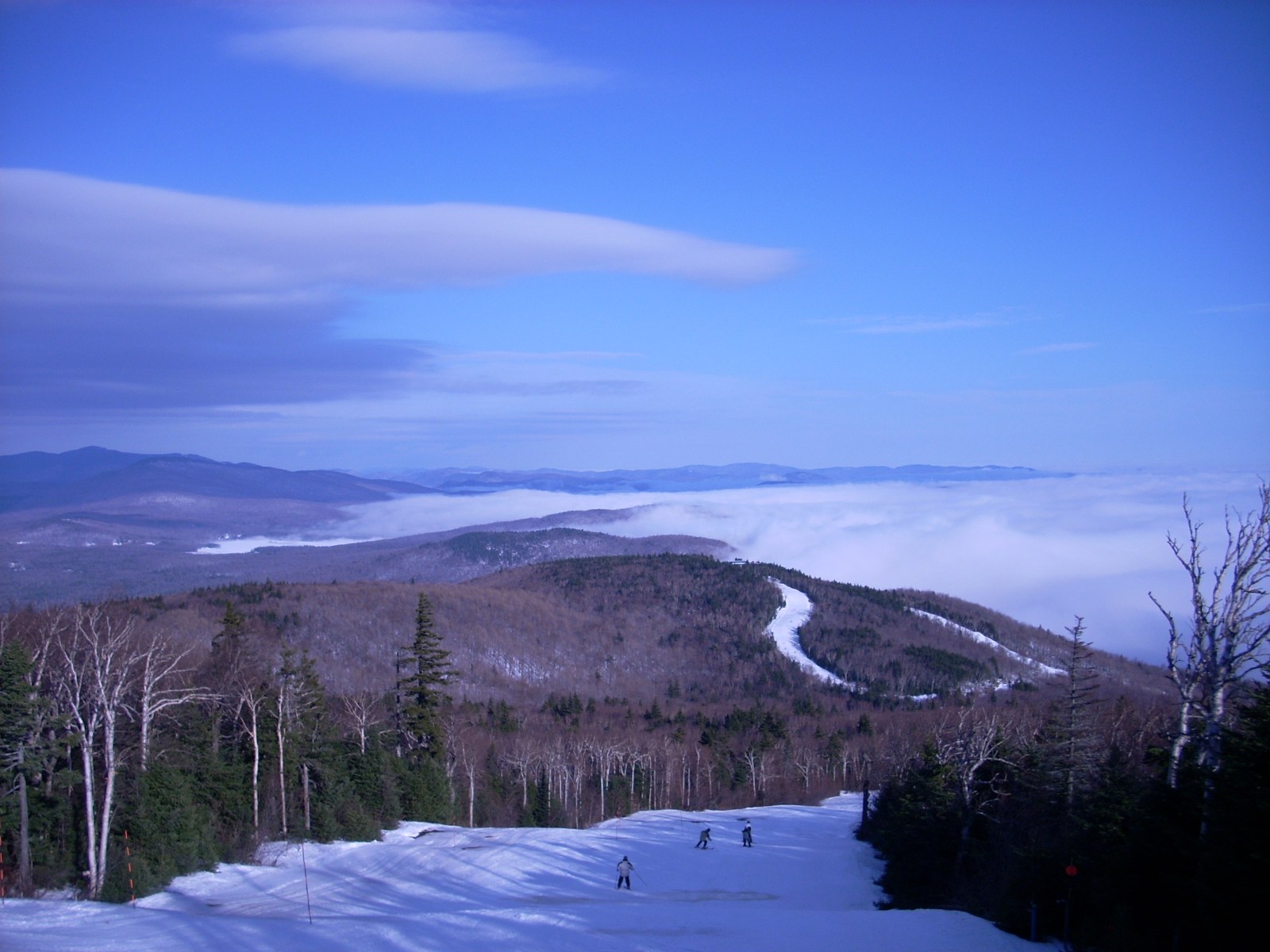 Skiers on a trail near the peak of Okemo above a sea of clouds